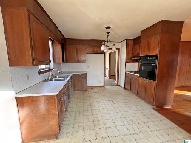 kitchen featuring black oven, backsplash, hanging light fixtures, sink, and a chandelier