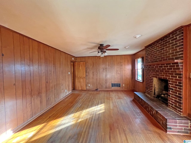 unfurnished living room featuring ceiling fan, wooden walls, a brick fireplace, and light hardwood / wood-style flooring