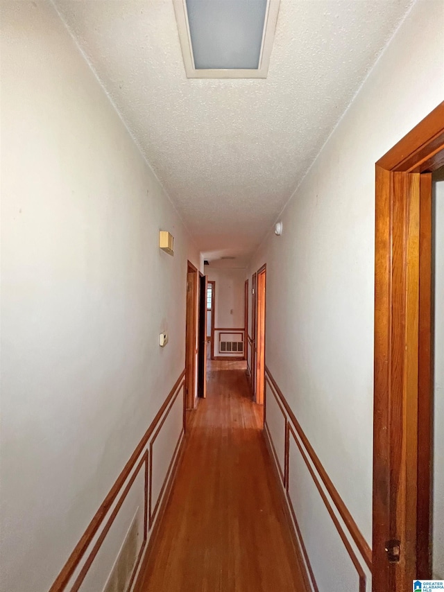 hall featuring a textured ceiling, wood finished floors, wainscoting, and a decorative wall