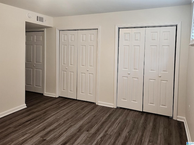 unfurnished bedroom featuring dark hardwood / wood-style floors and two closets