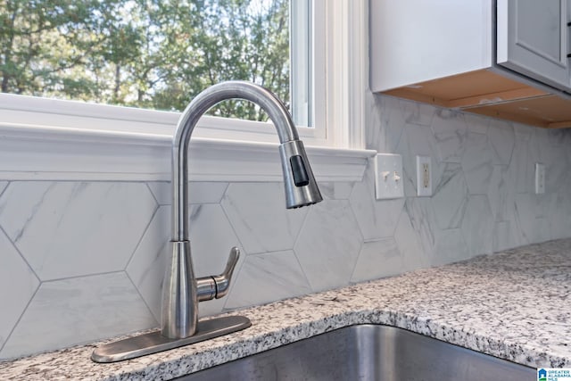 interior details featuring tasteful backsplash, light stone countertops, and sink