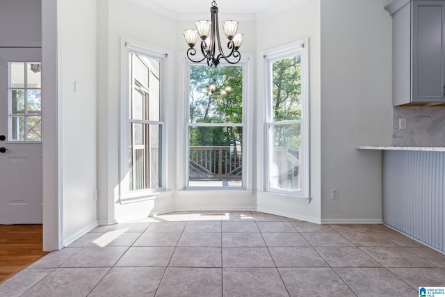 unfurnished dining area with light tile patterned floors, crown molding, and an inviting chandelier