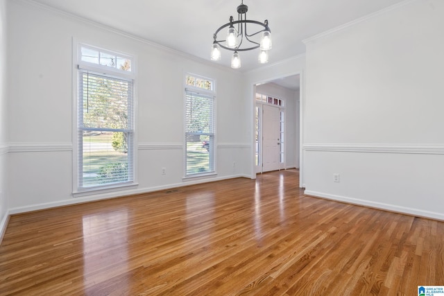 unfurnished room featuring ornamental molding, a wealth of natural light, hardwood / wood-style flooring, and an inviting chandelier