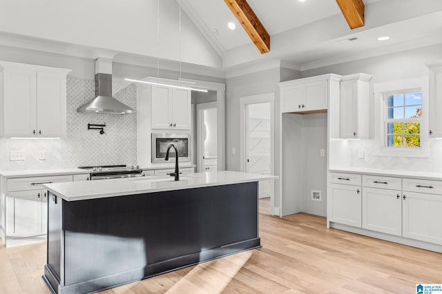 kitchen with white cabinetry, a center island with sink, lofted ceiling with beams, and wall chimney range hood