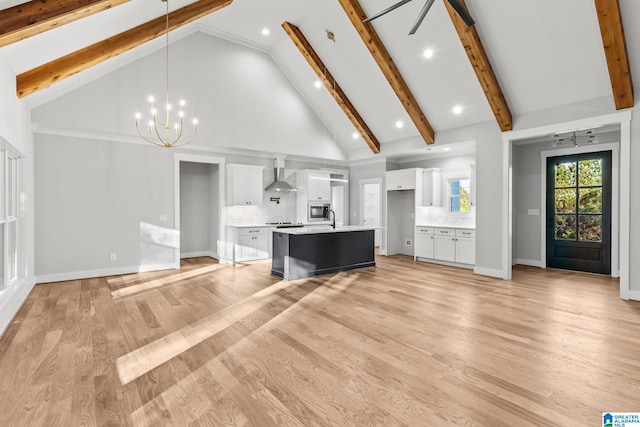 kitchen featuring wall chimney exhaust hood, decorative light fixtures, high vaulted ceiling, white cabinetry, and an island with sink