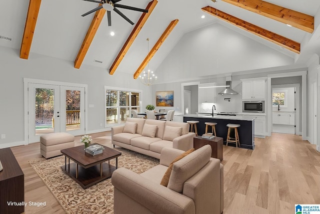 living room featuring high vaulted ceiling, french doors, ceiling fan with notable chandelier, light hardwood / wood-style flooring, and beam ceiling