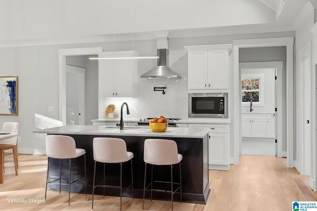 kitchen featuring white cabinetry, black microwave, a kitchen island with sink, and wall chimney range hood