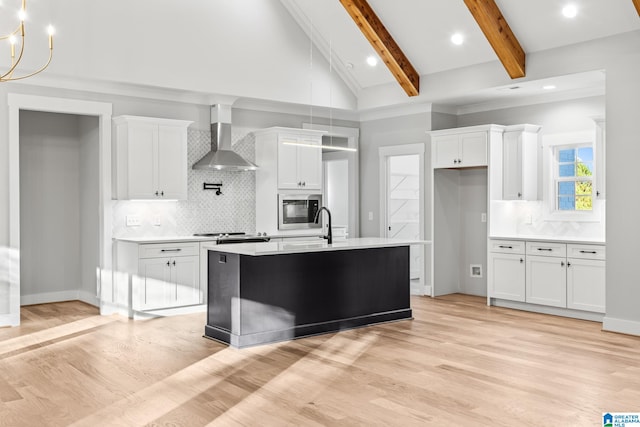 kitchen with white cabinetry, wall chimney range hood, beamed ceiling, high vaulted ceiling, and a kitchen island with sink