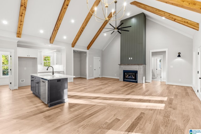 kitchen with high vaulted ceiling, a center island with sink, sink, a fireplace, and white cabinetry