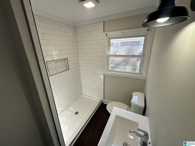 bathroom with toilet, a tile shower, and ornamental molding