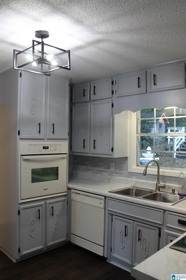 kitchen featuring white appliances, a sink, a textured ceiling, dark wood finished floors, and a chandelier