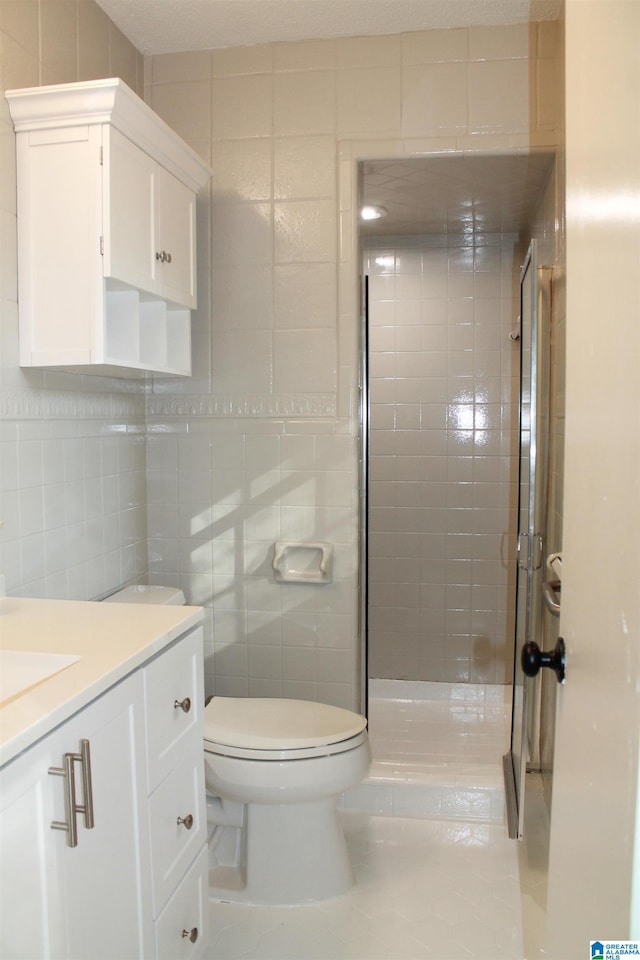 bathroom with tile patterned floors, tile walls, a stall shower, toilet, and vanity