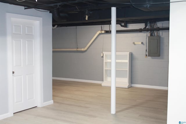 unfinished basement with electric panel, wood finished floors, concrete block wall, and baseboards