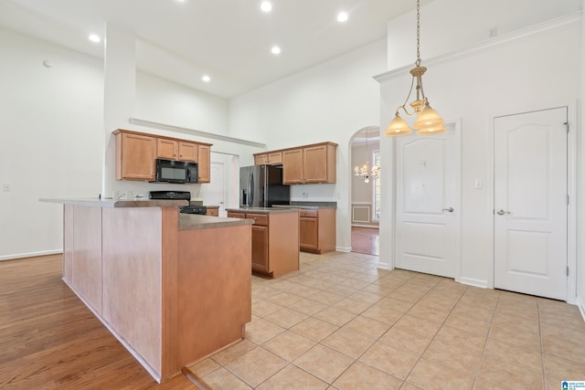 kitchen featuring a center island, a towering ceiling, hanging light fixtures, black appliances, and light tile patterned floors