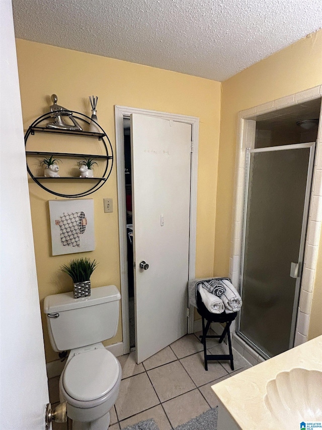 bathroom with sink, tile patterned floors, a textured ceiling, toilet, and a shower with door