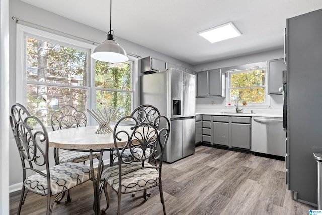 kitchen with hanging light fixtures, sink, gray cabinets, light wood-type flooring, and appliances with stainless steel finishes