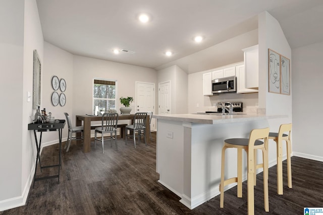 kitchen with stainless steel appliances, dark hardwood / wood-style flooring, a kitchen breakfast bar, white cabinets, and kitchen peninsula