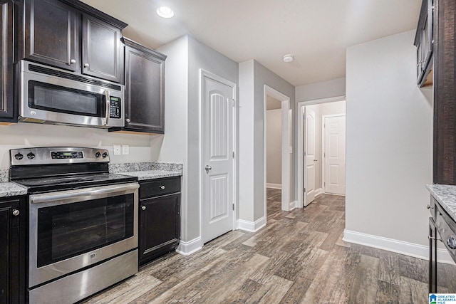 kitchen with dark brown cabinetry, light stone countertops, hardwood / wood-style floors, and stainless steel appliances