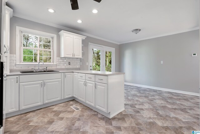 kitchen featuring decorative backsplash, kitchen peninsula, ornamental molding, sink, and white cabinets