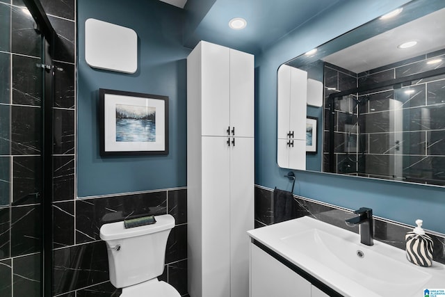 bathroom featuring a shower with shower door, vanity, toilet, and tile walls