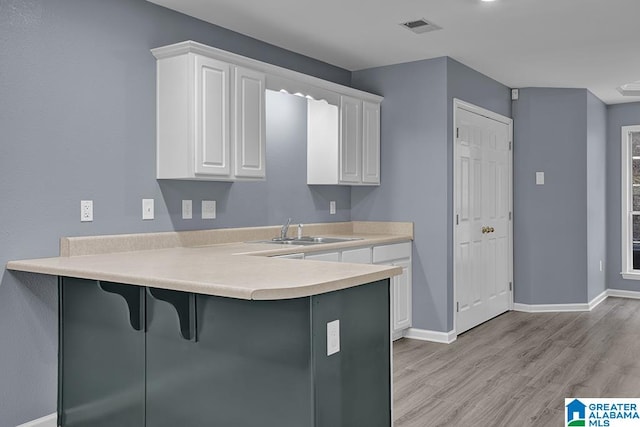 kitchen with white cabinets, kitchen peninsula, a kitchen breakfast bar, and light wood-type flooring