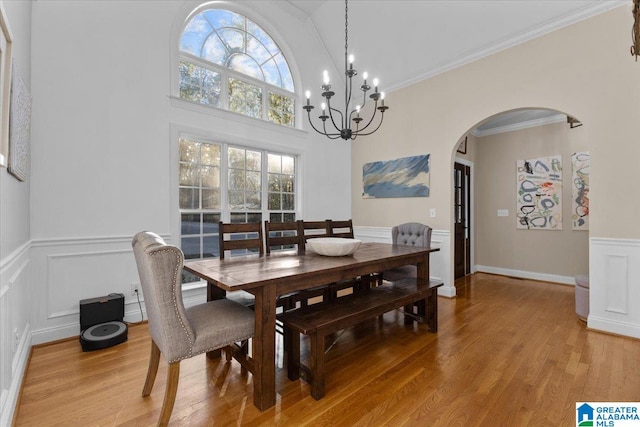 dining space with a towering ceiling, hardwood / wood-style flooring, ornamental molding, and a notable chandelier