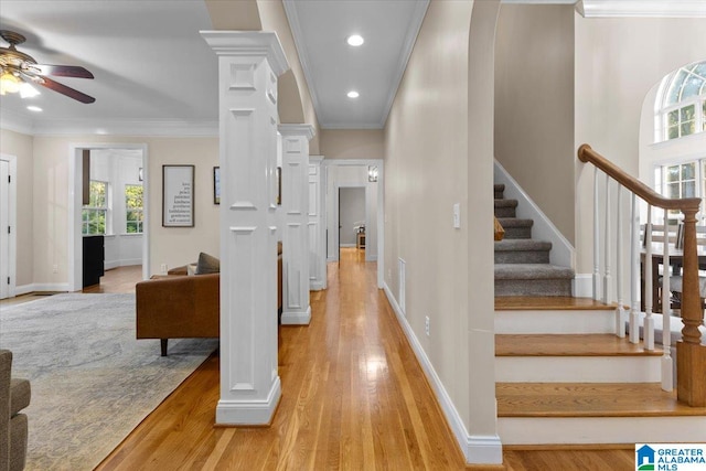 stairway with ceiling fan, wood-type flooring, crown molding, and decorative columns