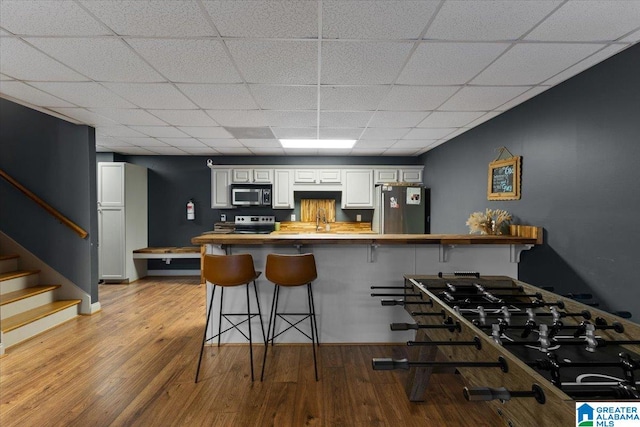 kitchen featuring a kitchen bar, a drop ceiling, kitchen peninsula, light hardwood / wood-style flooring, and appliances with stainless steel finishes