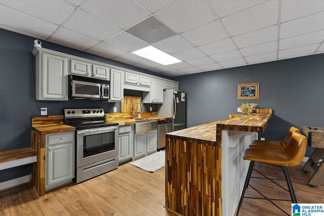 kitchen featuring stainless steel appliances, sink, a breakfast bar area, butcher block countertops, and light wood-type flooring