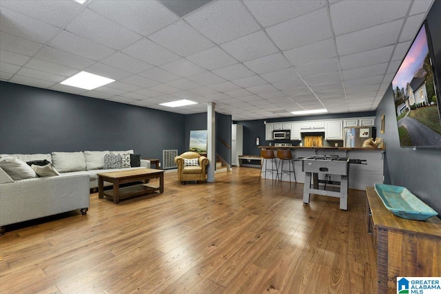 living room featuring light wood-type flooring and a drop ceiling