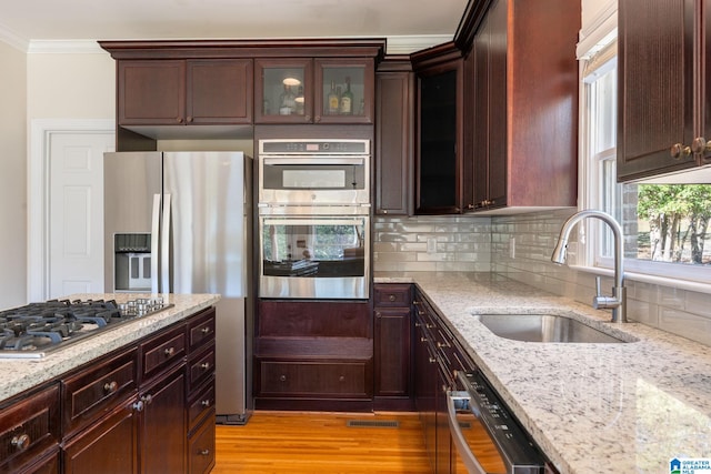 kitchen with stainless steel appliances, sink, crown molding, light stone countertops, and light hardwood / wood-style flooring