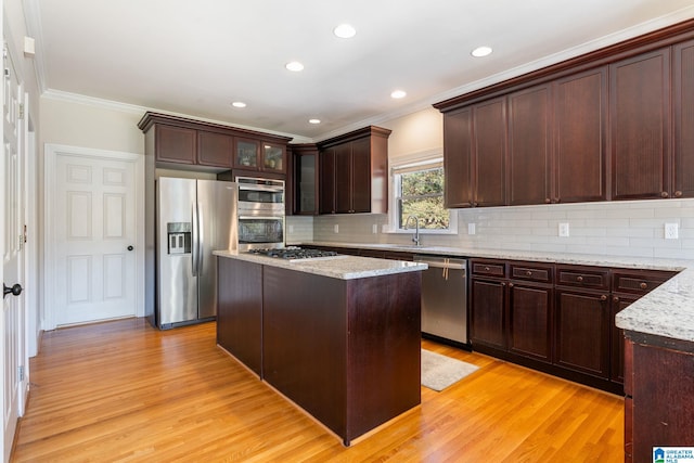 kitchen featuring light stone counters, appliances with stainless steel finishes, crown molding, a center island, and light wood-type flooring