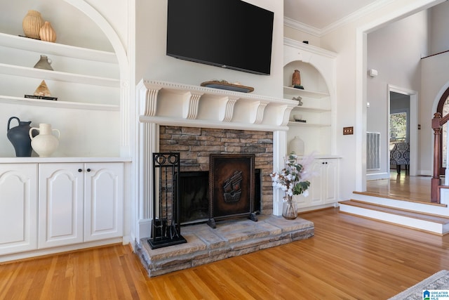 unfurnished living room featuring crown molding, light wood-type flooring, built in features, and a fireplace