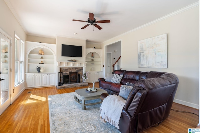 living room featuring ceiling fan, a fireplace, light hardwood / wood-style flooring, crown molding, and built in features