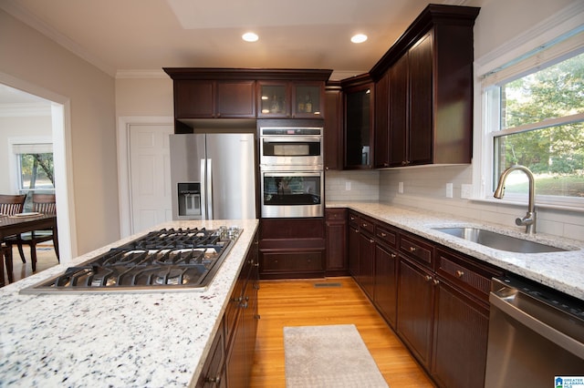 kitchen featuring sink, light stone counters, appliances with stainless steel finishes, backsplash, and light wood-type flooring