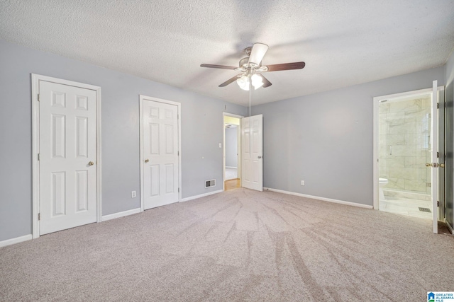 unfurnished bedroom with ensuite bath, ceiling fan, a textured ceiling, carpet floors, and two closets