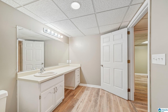 bathroom with toilet, a drop ceiling, vanity, and hardwood / wood-style floors