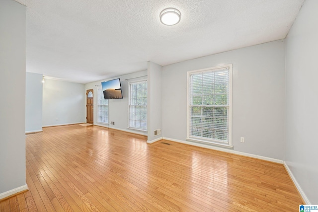 unfurnished living room with a textured ceiling and light hardwood / wood-style floors