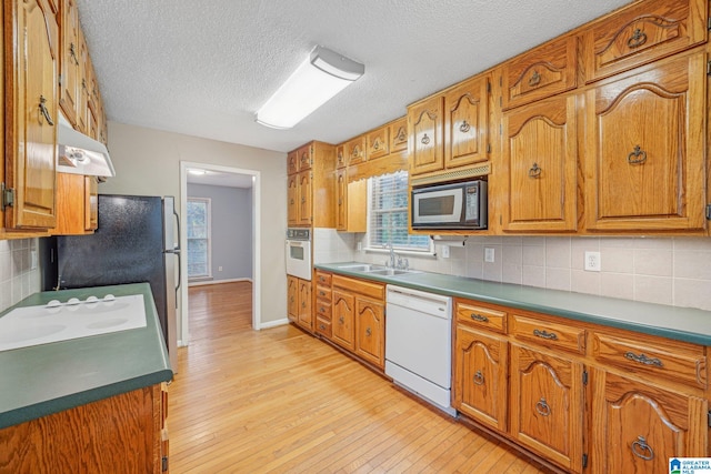 kitchen featuring sink, a textured ceiling, white appliances, light hardwood / wood-style flooring, and decorative backsplash