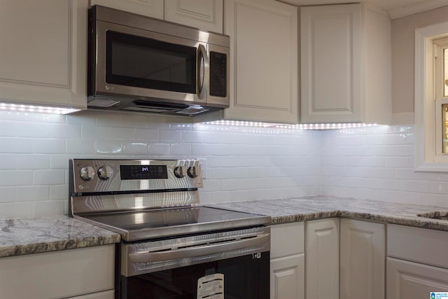 kitchen featuring white cabinetry, appliances with stainless steel finishes, backsplash, and light stone countertops