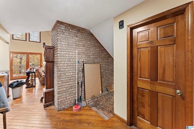 corridor with light wood-type flooring, brick wall, and lofted ceiling