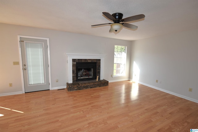 unfurnished living room with ceiling fan, light wood-type flooring, a textured ceiling, and a brick fireplace