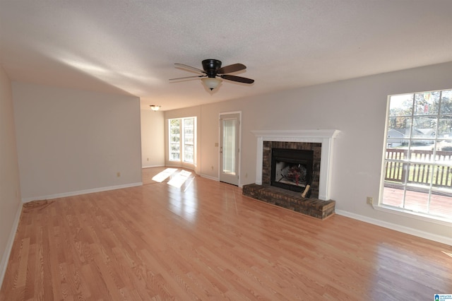 unfurnished living room featuring a fireplace, a textured ceiling, light wood-type flooring, and ceiling fan