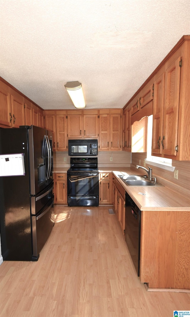 kitchen featuring sink, black appliances, a textured ceiling, and light hardwood / wood-style floors