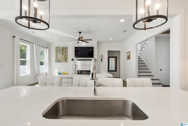 kitchen featuring a fireplace, sink, crown molding, and ceiling fan