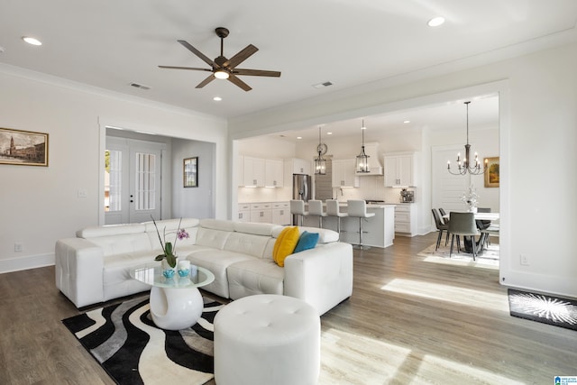 living room with ceiling fan with notable chandelier, wood-type flooring, and crown molding