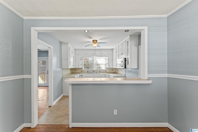 kitchen with crown molding, wood-type flooring, white cabinetry, and kitchen peninsula