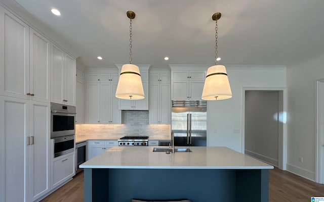 kitchen featuring stainless steel appliances, a kitchen island with sink, sink, hardwood / wood-style flooring, and hanging light fixtures