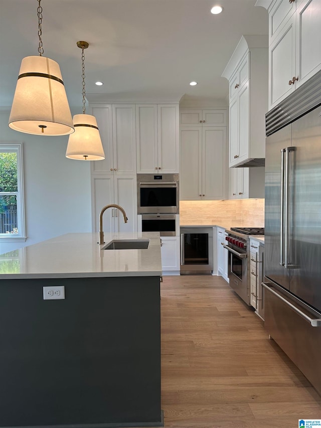 kitchen featuring light wood-type flooring, a kitchen island with sink, high quality appliances, white cabinetry, and hanging light fixtures