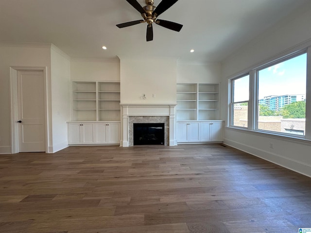 unfurnished living room with built in shelves, dark hardwood / wood-style floors, ceiling fan, and crown molding